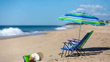 Escena de playa con un paraguas de rayas, una silla de playa azul y blanca a rayas, y un balón de playa verde y azul sobre la arena.