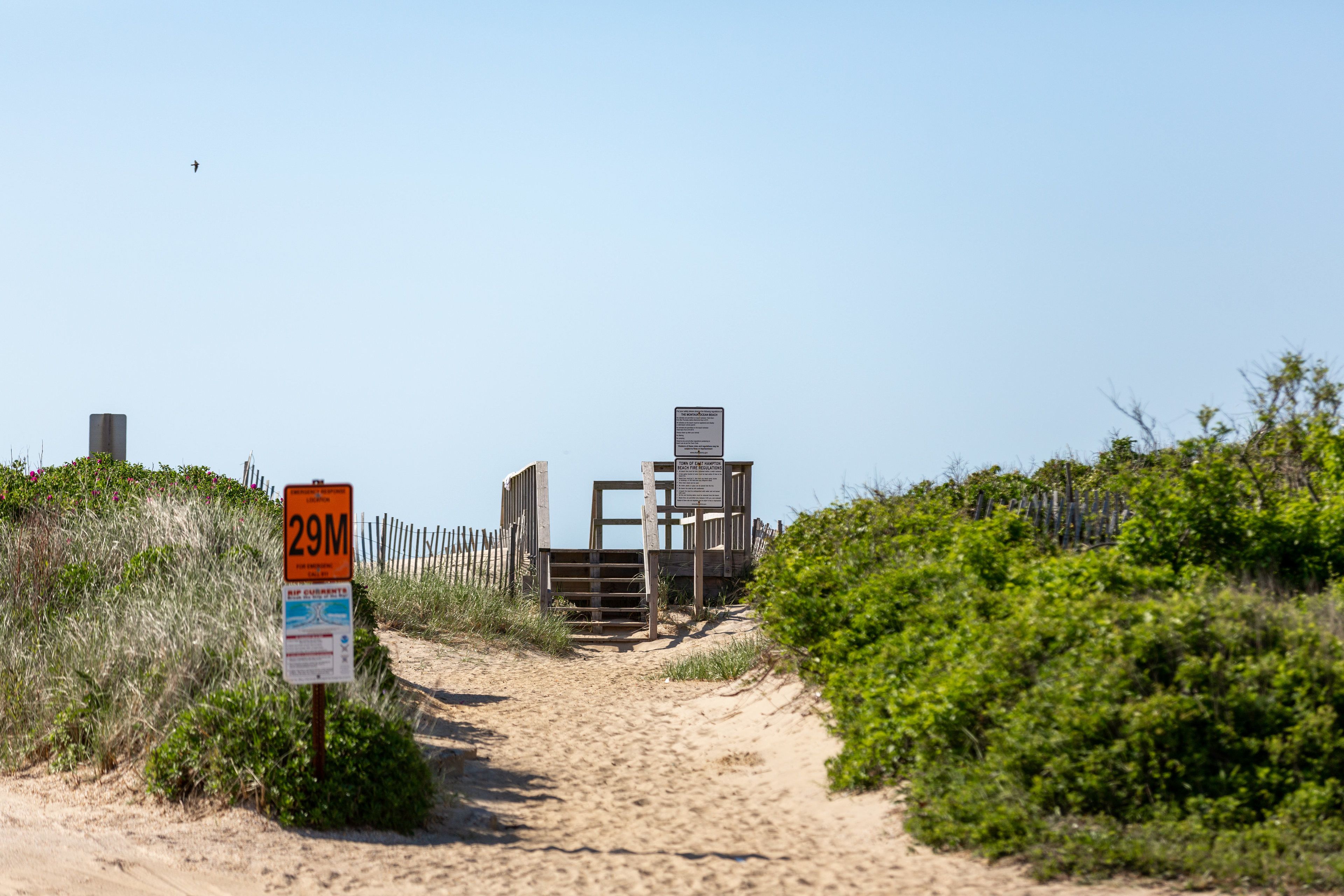 A sandy beach path leading to a wooden gate with a sign indicating a 29-meter distance.