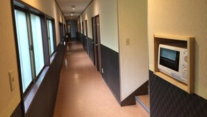 A long, narrow hotel corridor with doors on both sides, a microwave on the right wall, and a light-colored carpet. - Hotel Famitic Myojin (Nikko)