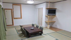 A room with tatami flooring, a wooden table with cushions, a television on a shelf, and a door. - Hotel Famitic Myojin (Nikko)