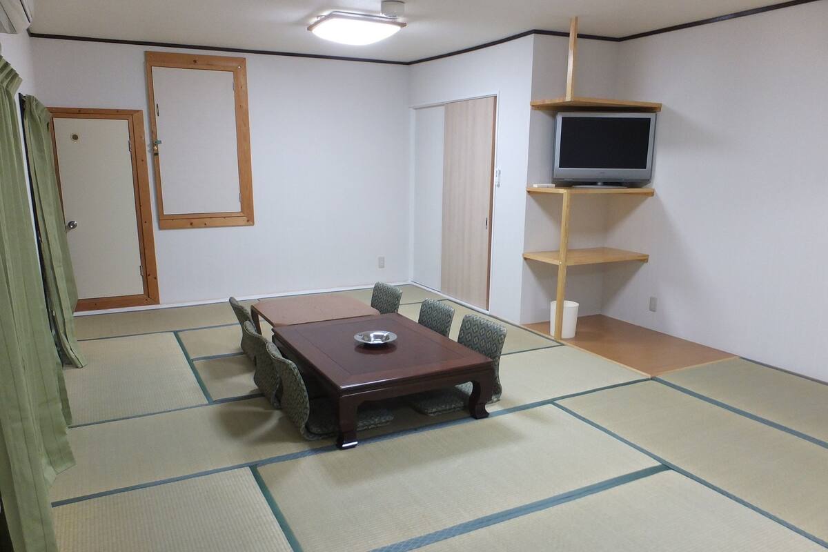 A room with tatami flooring, a wooden table with cushions, a television on a shelf, and a door.
