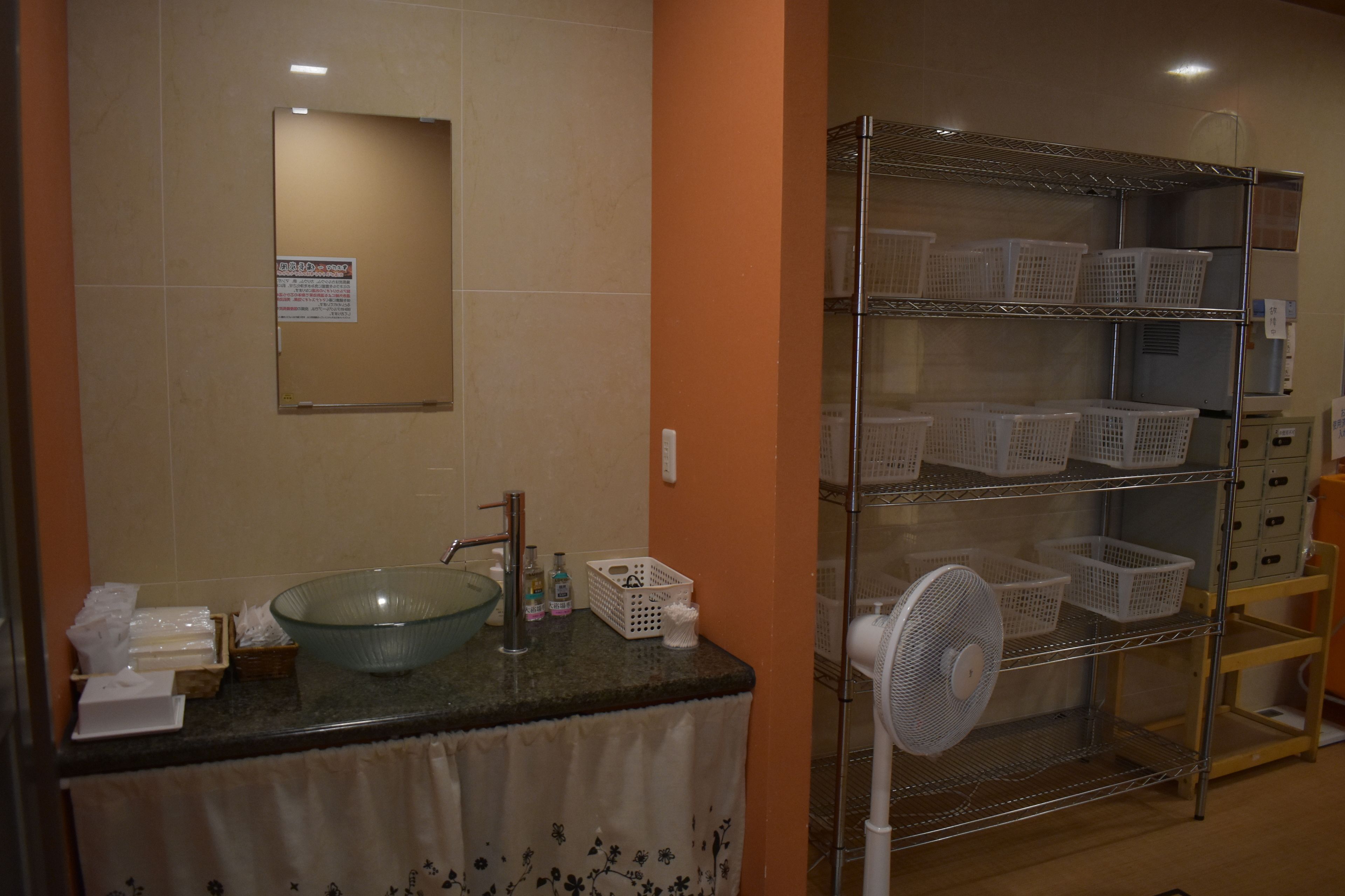 Un baño con lavamanos de cristal, un espejo y una repisa con cestas.