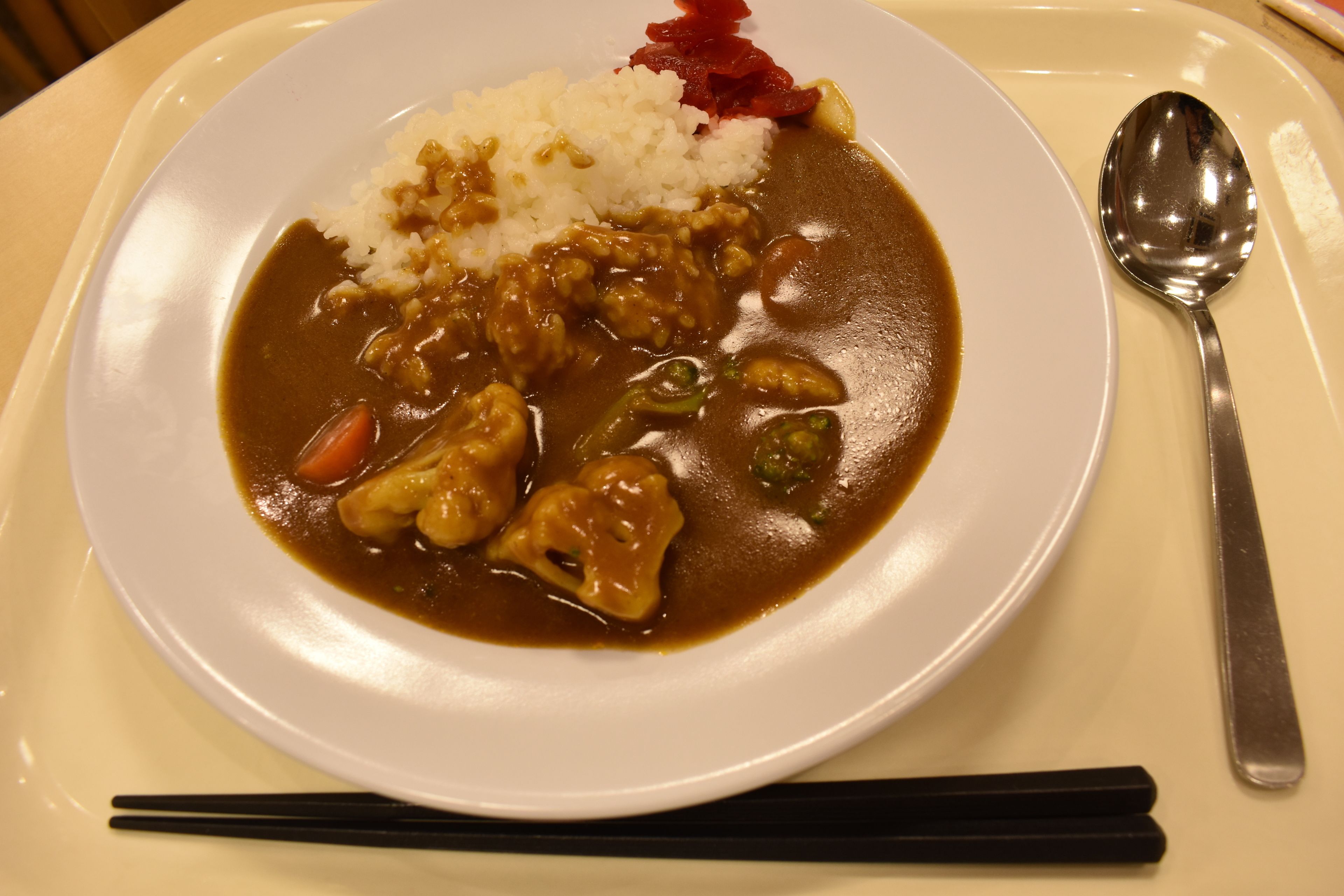 Un plato de curry con arroz y verduras, una cuchara y palillos sobre una mesa.