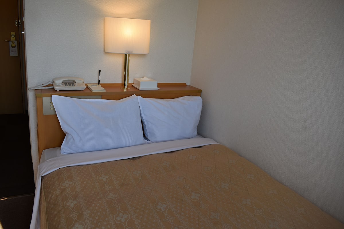 Een hotelkamer met een bed, een bedlampje, een telefoon en een notitieboekje op het nachtkastje.