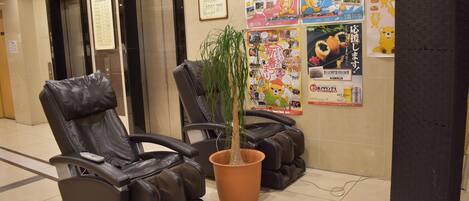 Een massageruimte met twee massagestoelen, een potplant en informatieposters aan de muur.