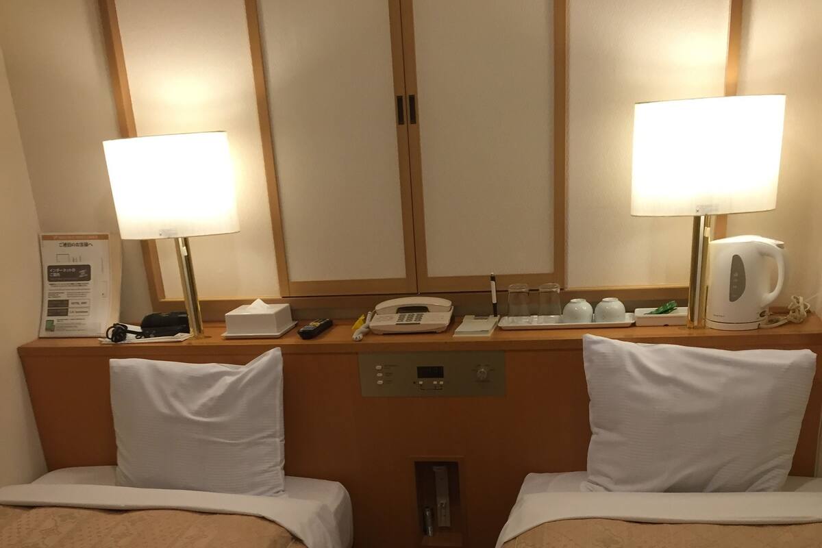 Een hotelkamer met twee bedden, een nachtkastje met een lamp, een telefoon en een koffiezetapparaat.