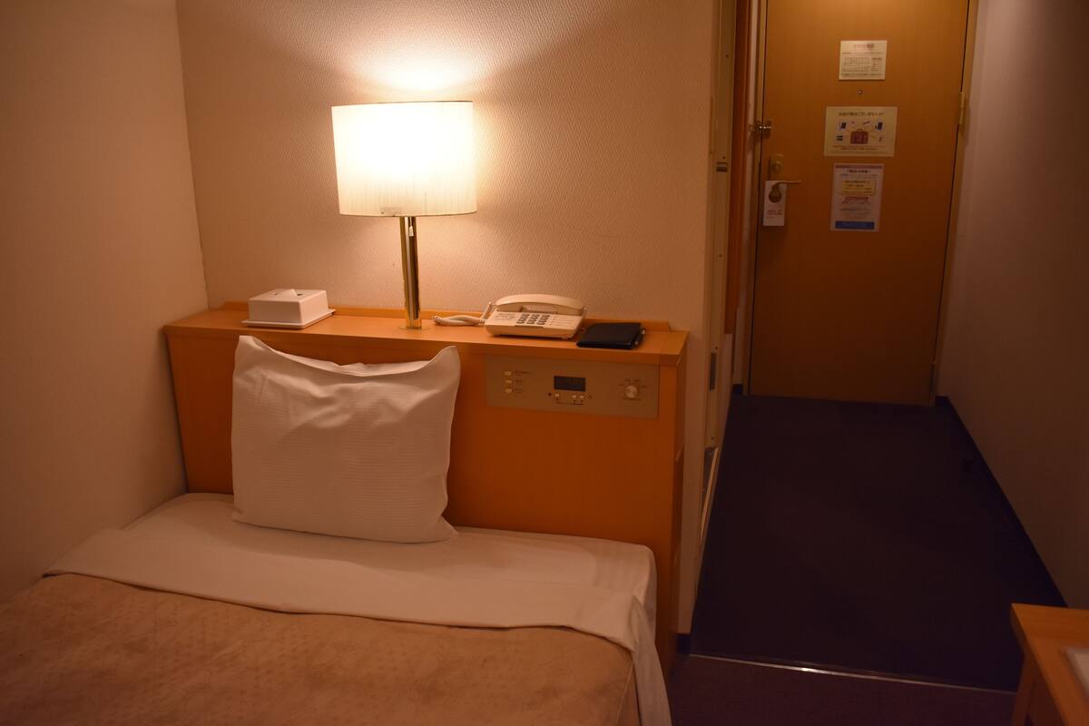 Hotelkamer met een bed, nachtkastje met een lamp, telefoon en een deur met bordje.