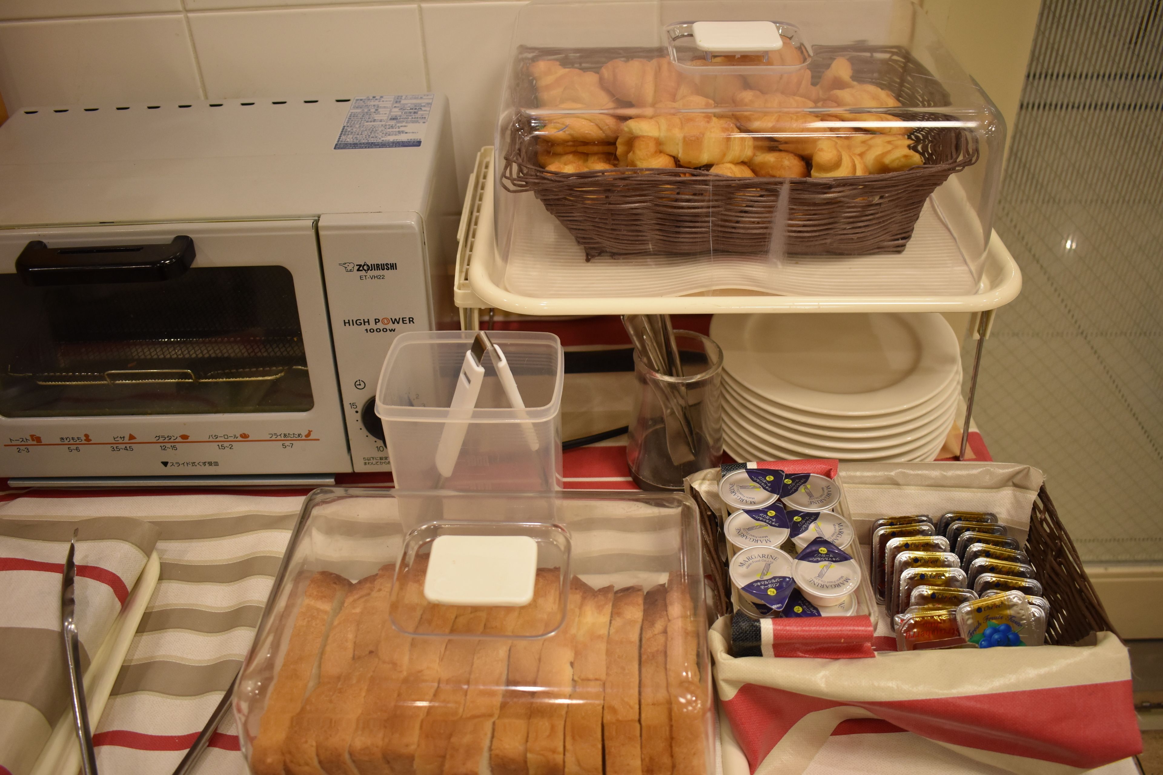 Una mesa de desayuno buffet con panes, bollería y salsas.