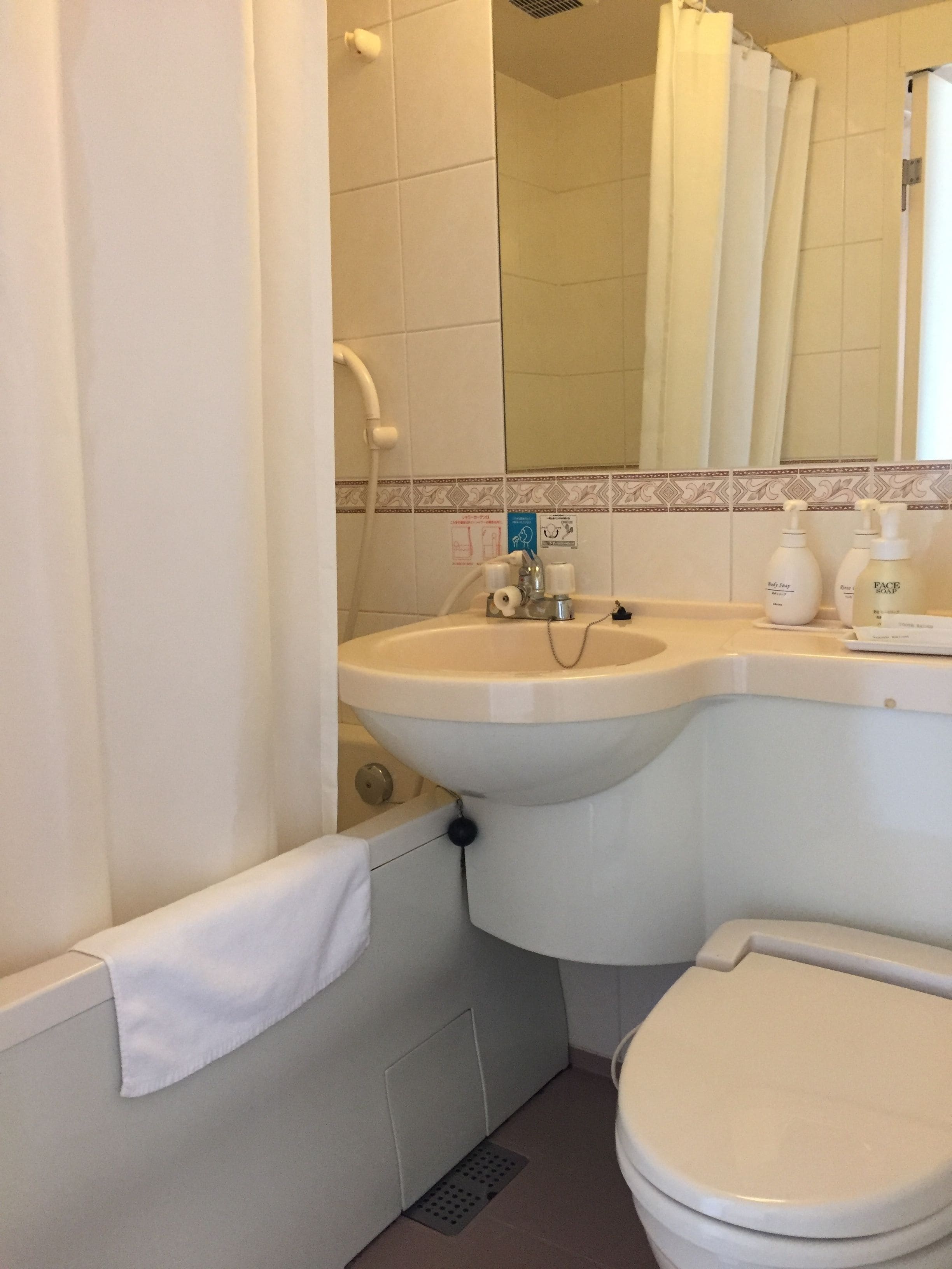 Un baño con lavamanos, inodoro y bañera. Hay artículos de aseo en la encimera del lavamanos.