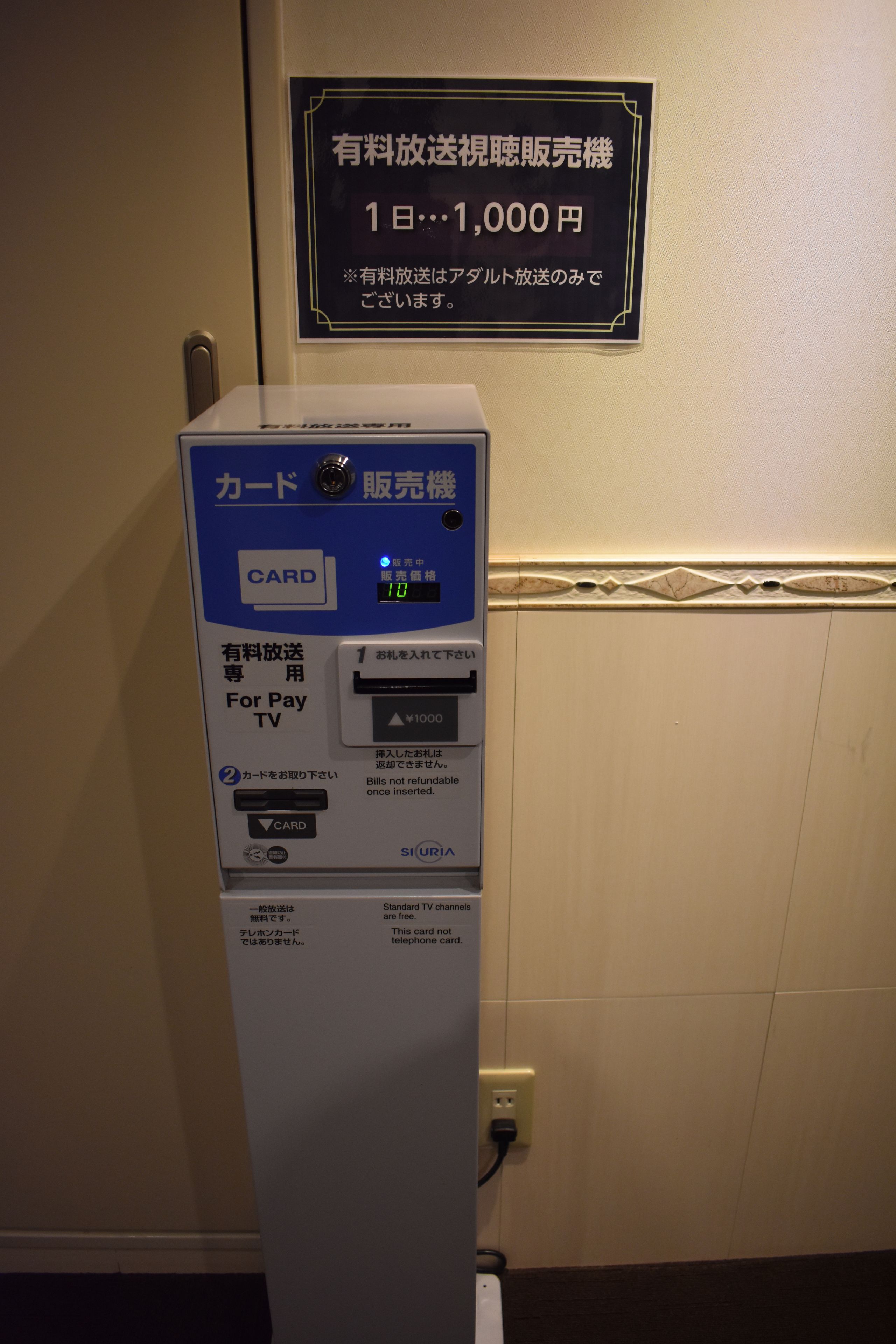 A pay TV card vending machine with a sign above it indicating a 1,000 yen fee for card delivery.