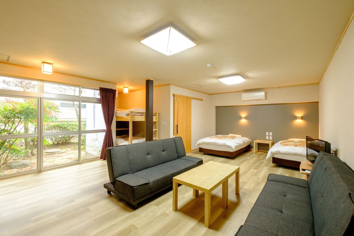 A modern hotel room with a sofa, a bed, a small table, and a large window offering a view of the outdoors.