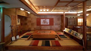 Una habitación tradicional con tatamis, una mesa de tatamis, una estantería con libros y un techo con vigas de madera.