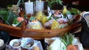 Una comida tradicional japonesa dispuesta con una barca de madera, varios platos y una pequeña mesa con cuencos y platos.