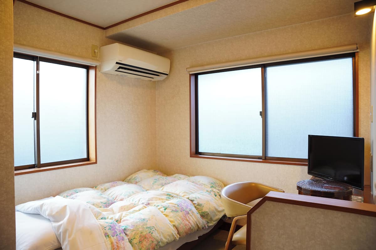 A hotel room with a bed, a chair, a television, and large windows.