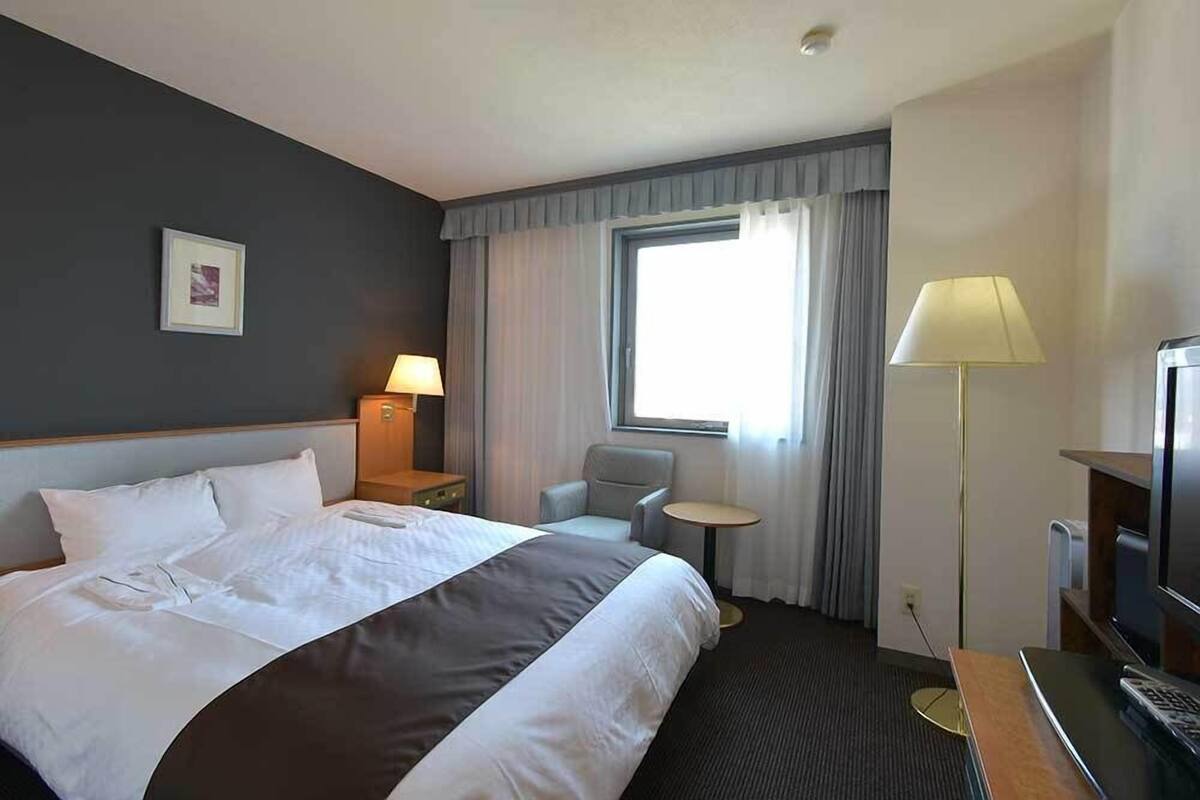 Una habitación de hotel con una cama grande, un escritorio, una silla, un televisor y una ventana con cortinas.