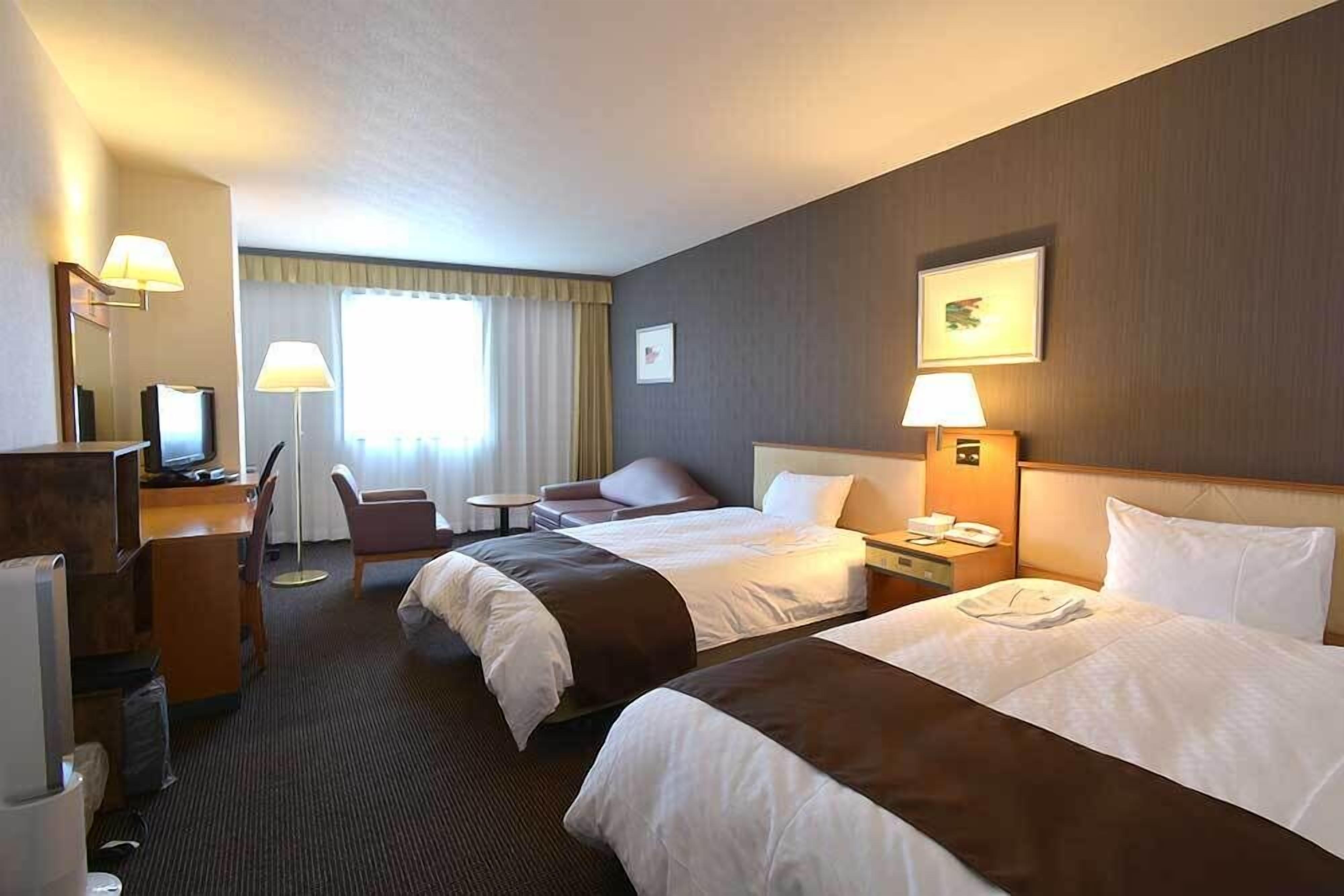 Habitación de hotel con dos camas, un escritorio con computadora, una silla, una mesita y una lámpara.