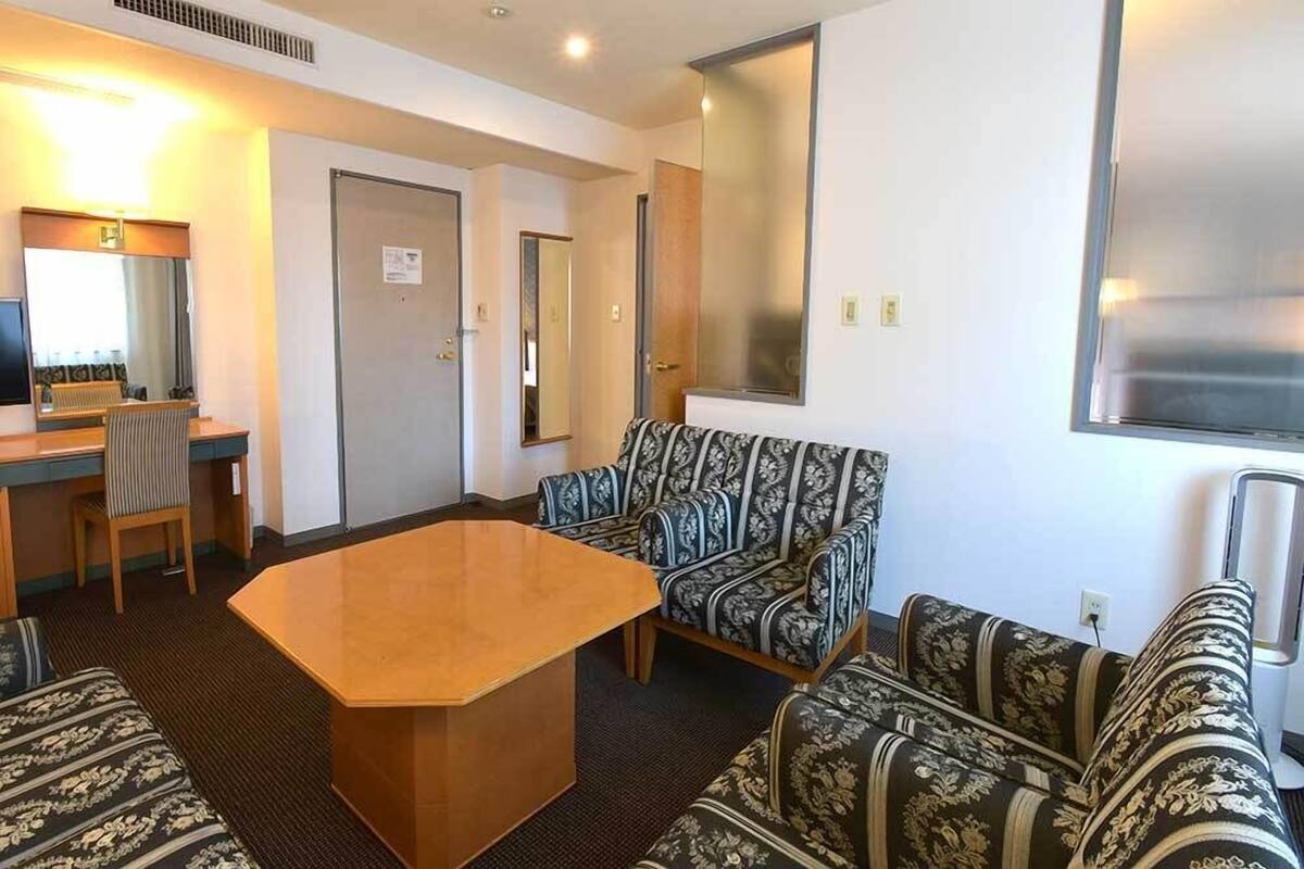 Una habitación de hotel con un escritorio de madera, dos sofás estampados, un espejo grande y una puerta.