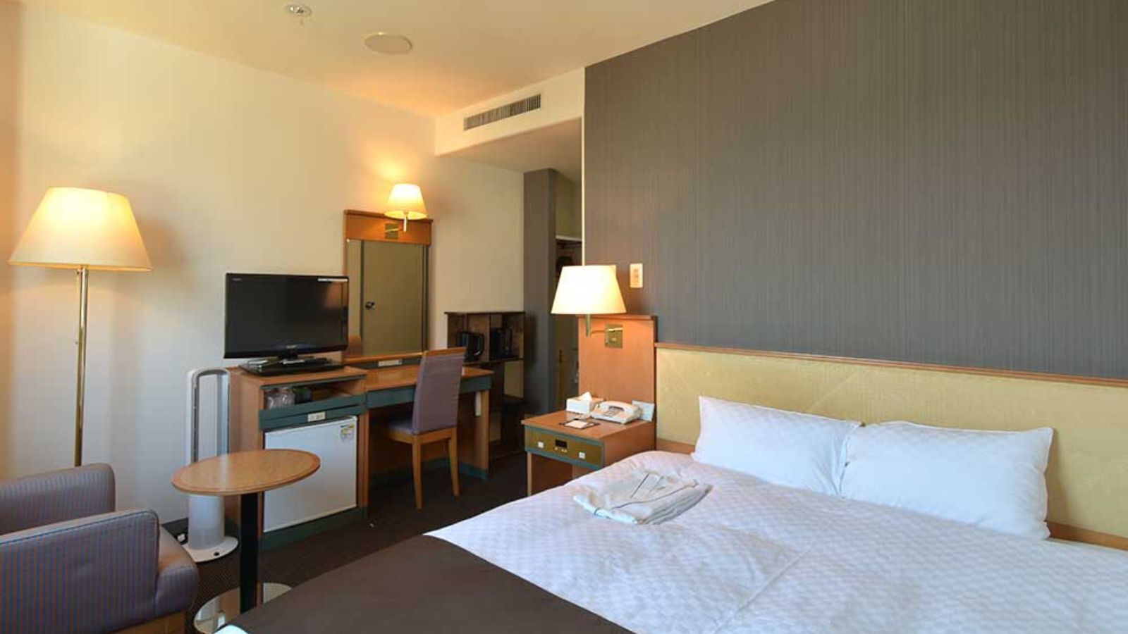 Habitación de hotel con cama, escritorio, silla, televisión y una pequeña kitchenette.