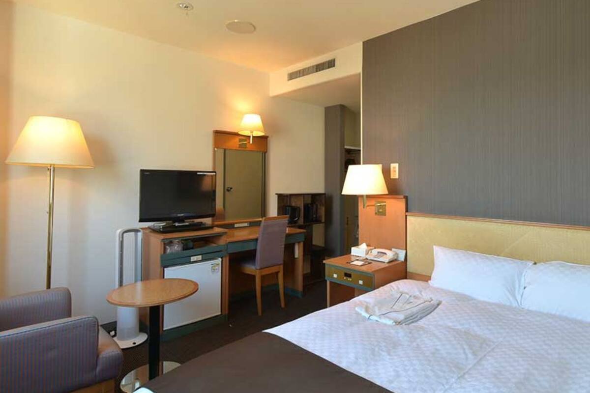 Habitación de hotel con cama, escritorio, silla, televisión y una pequeña kitchenette.