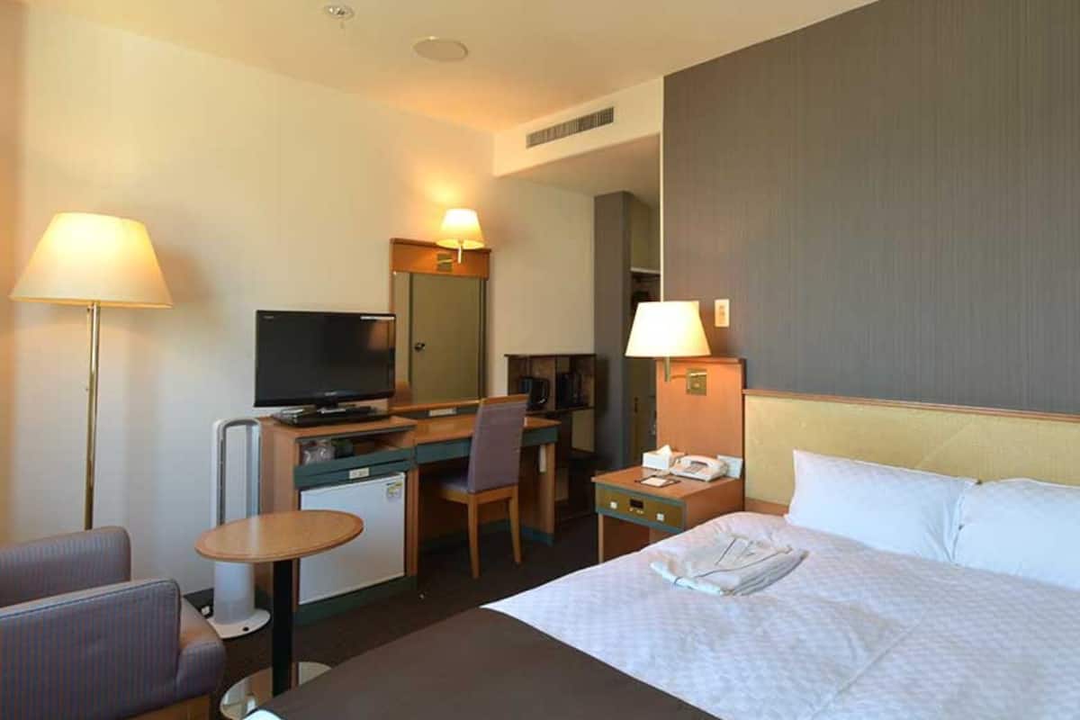 Habitación de hotel con cama, escritorio, silla, televisión y una pequeña kitchenette.