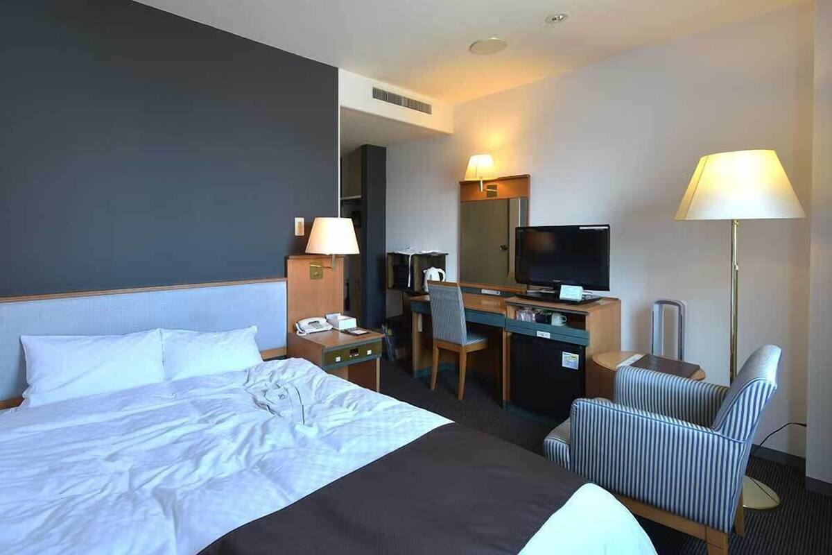 Una habitación de hotel con cama, escritorio, silla, televisión, lámpara y teléfono.