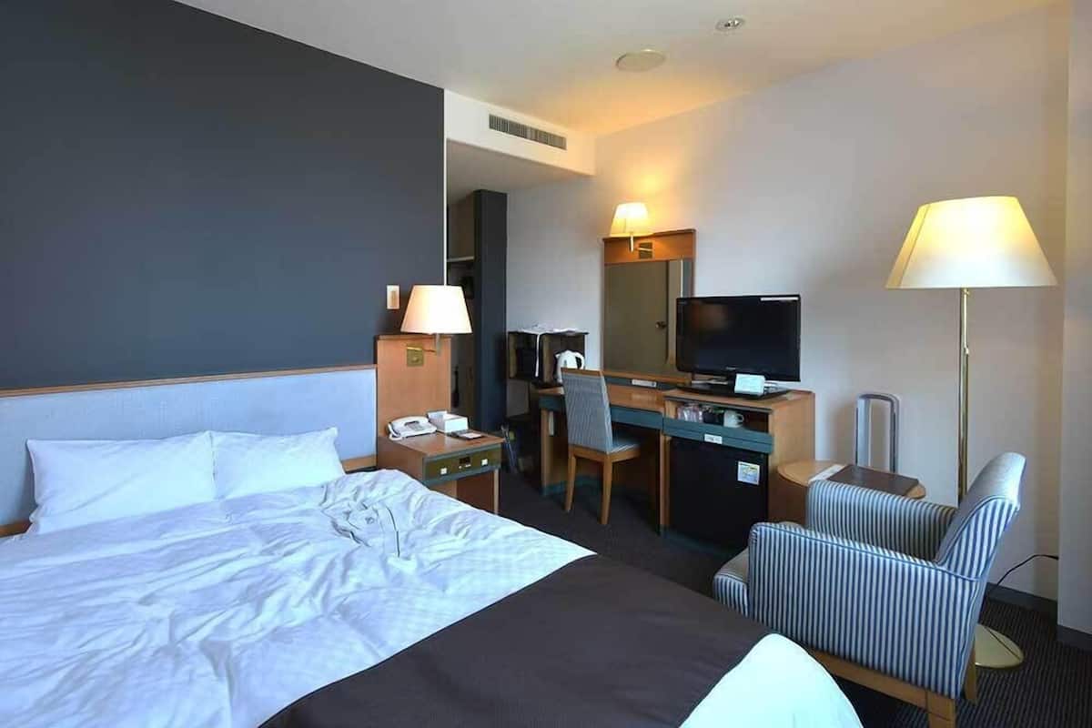 Una habitación de hotel con cama, escritorio, silla, televisión, lámpara y teléfono.