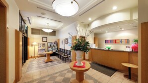 Un espace d’accueil comprenant un comptoir d’enregistrement, un coin salon avec des chaises, un vase décoratif avec des fleurs et un sol carrelé.
