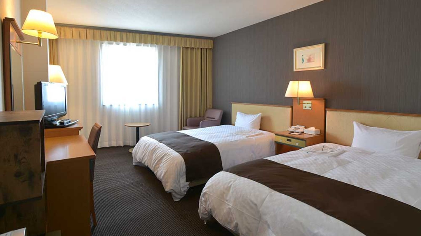 Habitación de hotel con dos camas, un escritorio, una silla, un televisor y una ventana con cortinas.