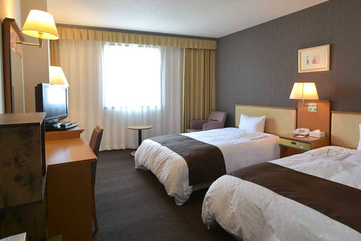 Habitación de hotel con dos camas, un escritorio, una silla, un televisor y una ventana con cortinas.