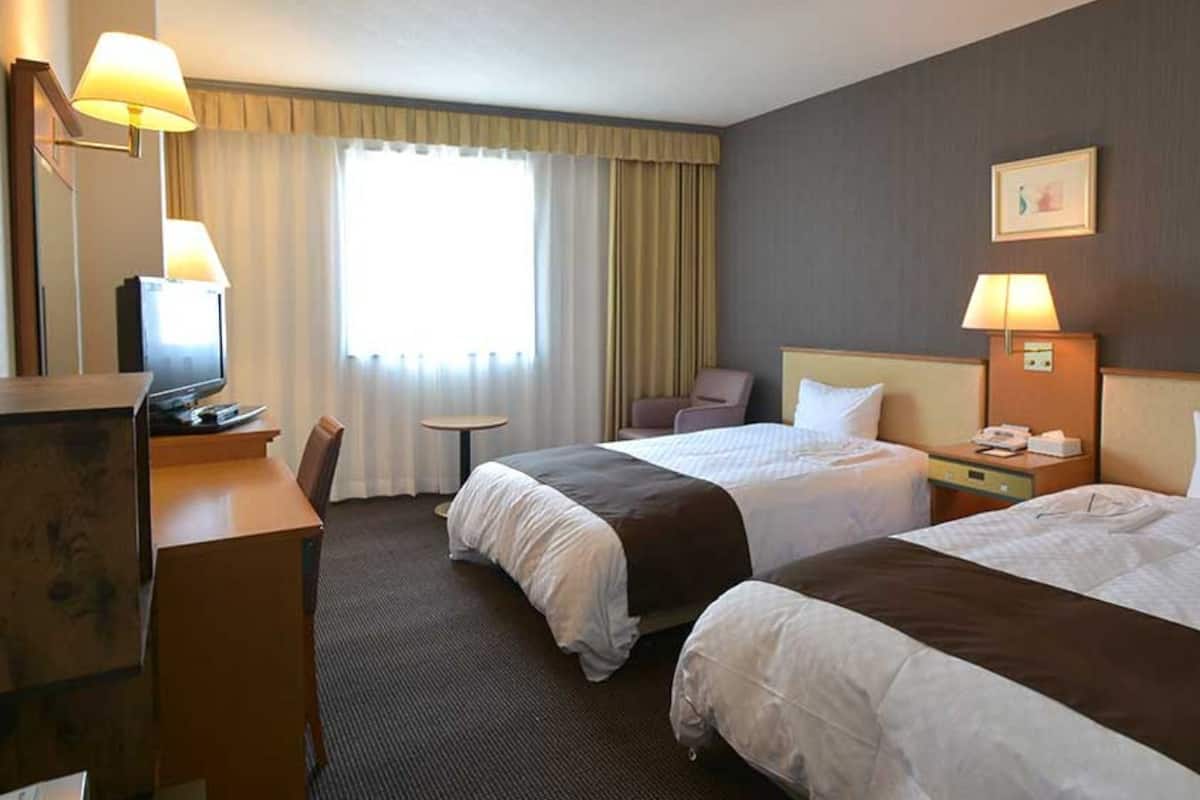Habitación de hotel con dos camas, un escritorio, una silla, un televisor y una ventana con cortinas.