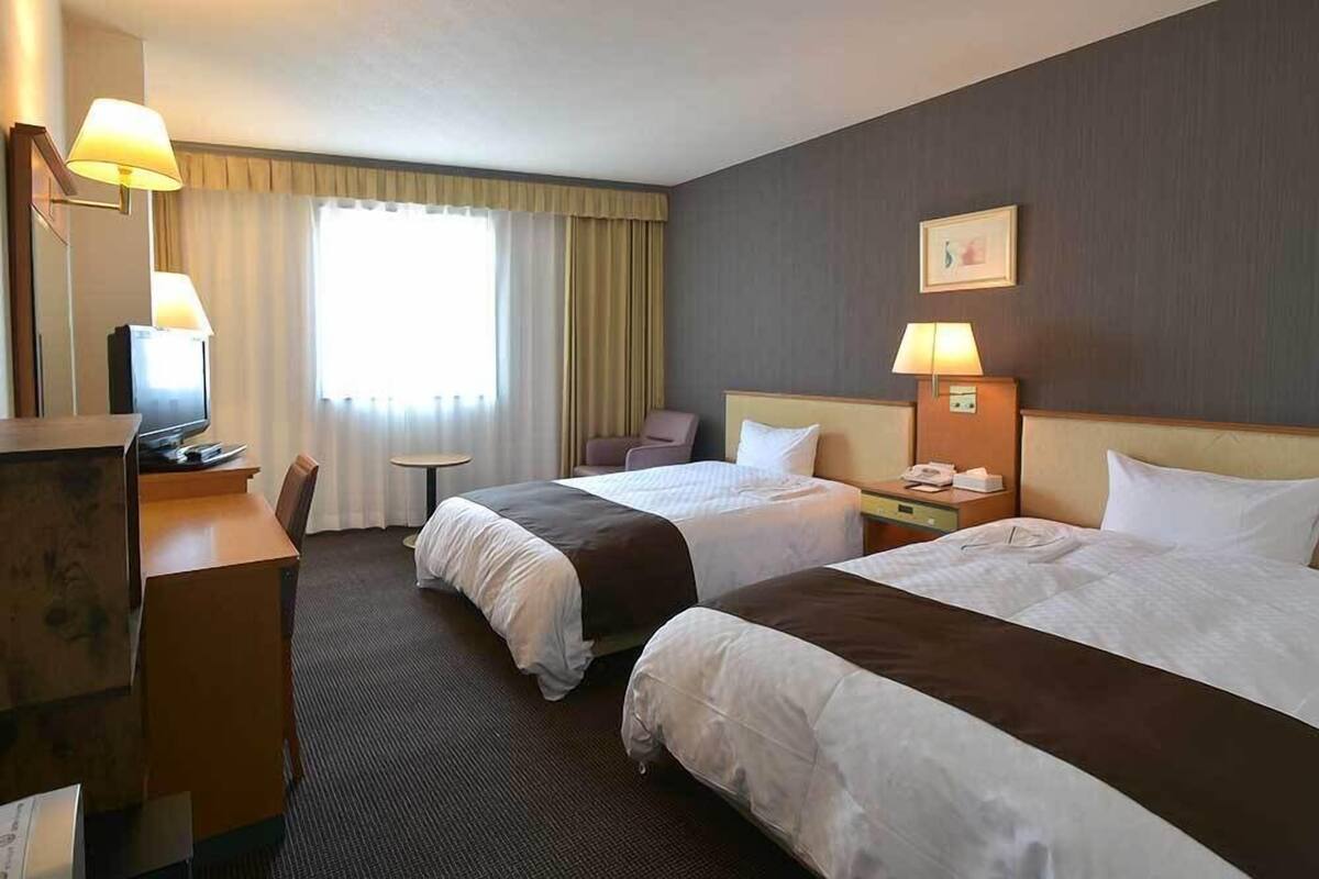 Habitación de hotel con dos camas, un escritorio, una silla, una mesita y un televisor.