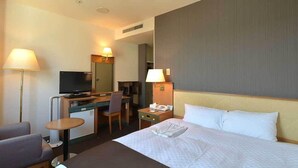 Une chambre d’hôtel comprenant un lit, un bureau avec une chaise, une télévision, une petite table et une lampe.