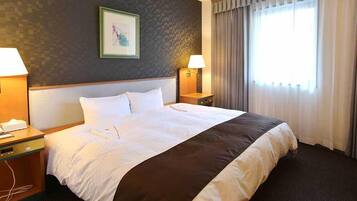 A hotel room with a large bed, two bedside tables, a wall-mounted lamp, a framed picture, and a window with curtains.