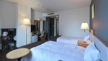 A hotel room with two beds, a desk, a chair, a lamp, and a small table.