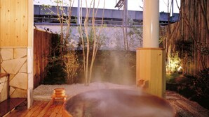 A hot tub on a wooden deck with a stone wall and bamboo fence in the background. - Kansuitei Kozeniya (Tottori)