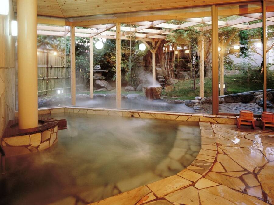 A hot spring area with stone flooring, wooden seating, and a wooden pergola structure.