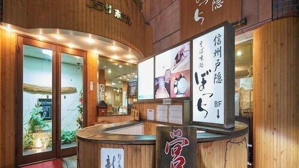 A wooden reception desk with Japanese signage, a red mat at the entrance, and a view into the interior of the building. - Nagano Plaza Hotel (Nagano)