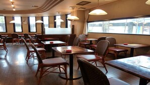 En restauranginteriör med träbord och stolar, stora fönster och hängande lampor.