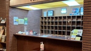 Ett receptionsområde med en skylt som visar ”ENTRÉ”, en disk med en glasvägg, ett litet bord med en flaska och en vägg av tegelstenar.