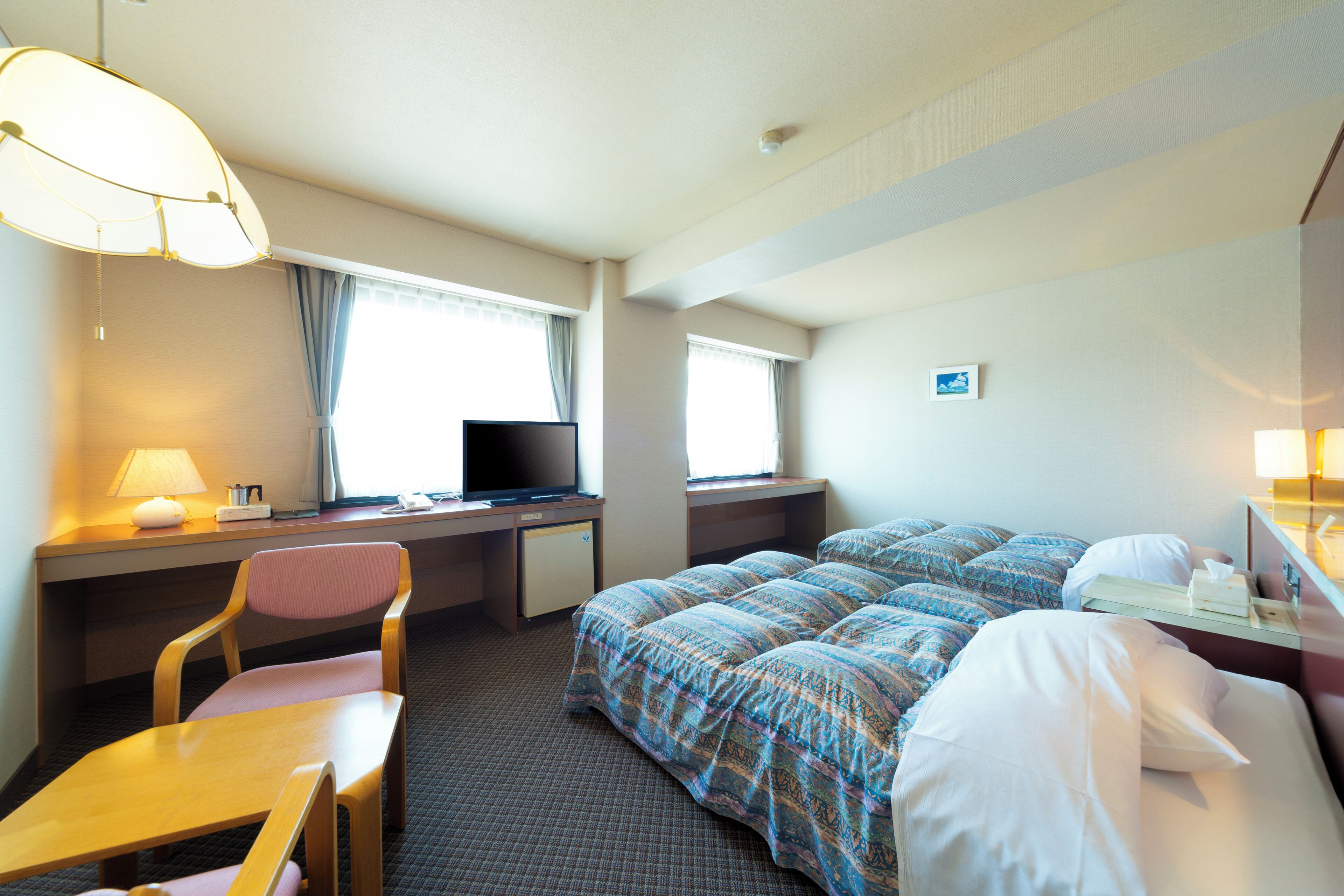 Habitación de hotel con cama, escritorio, silla, televisor y ventana con cortinas.