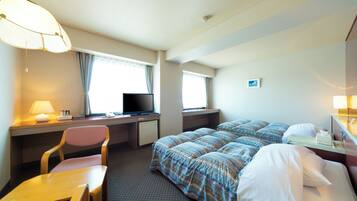 Habitación de hotel con cama, escritorio, silla, televisor y ventana con cortinas.