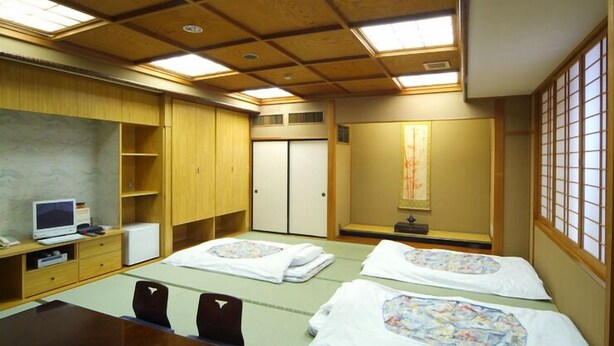 Ett traditionellt japanskt rum med tatamimattor på golvet, ett skrivbord i trä, en tv och en säng med ett blommigt överkast.