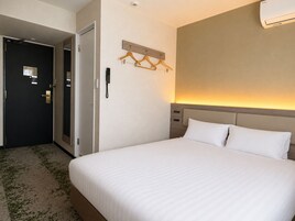 A hotel room with a bed, a bedside table, a wall-mounted phone, and a door.