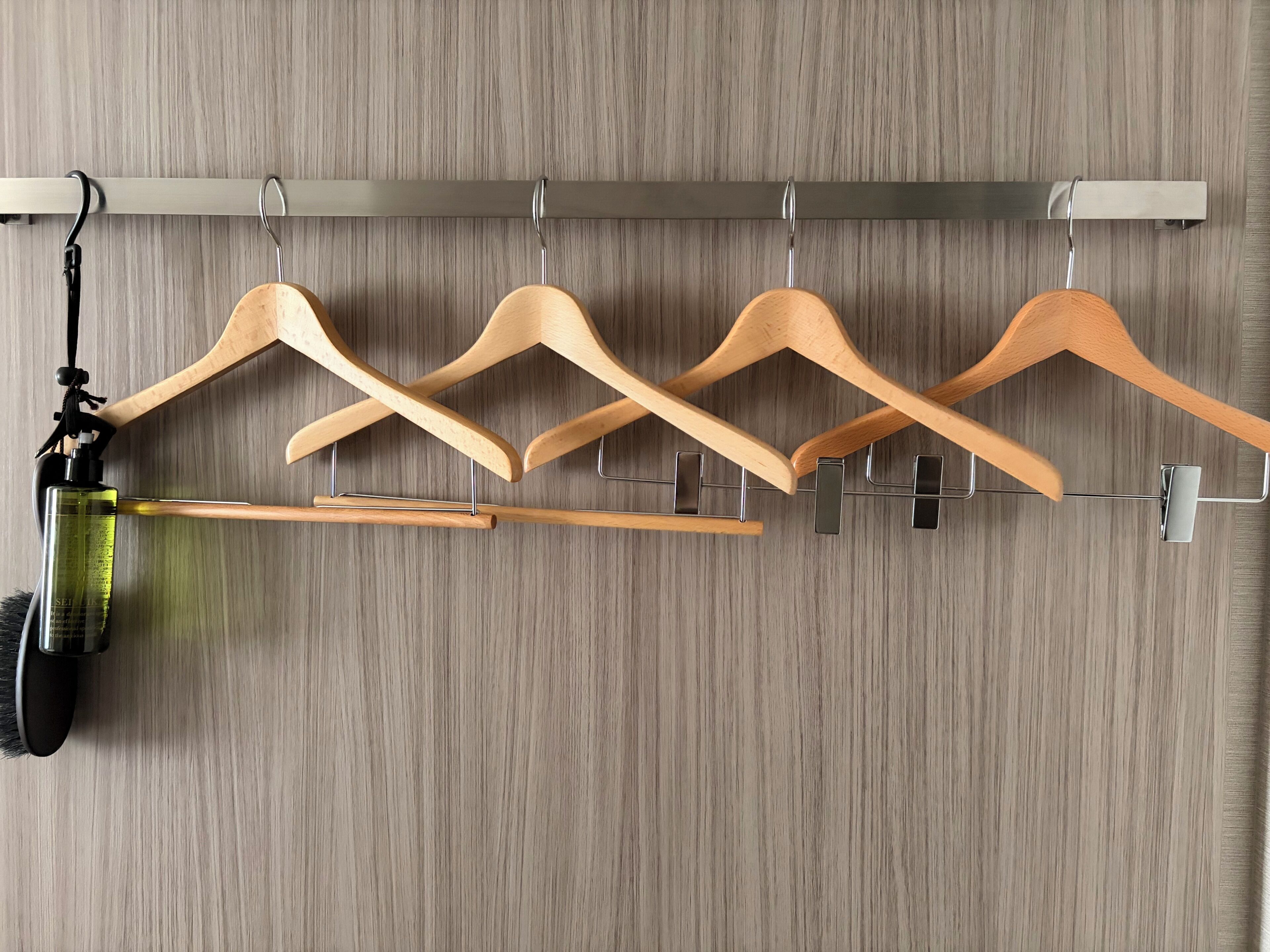 A wooden hanger rack with multiple hangers against a wooden wall.