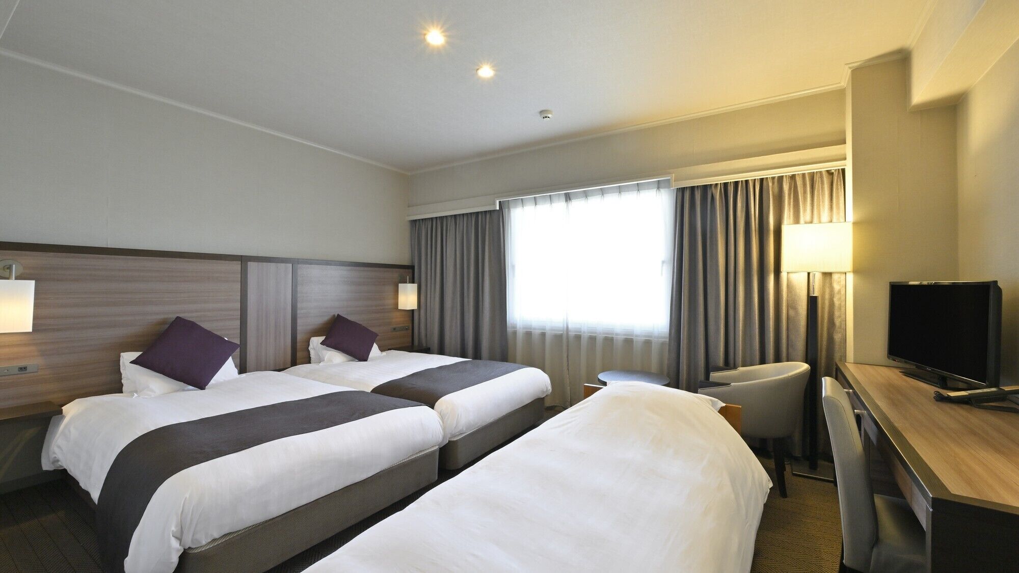 A hotel room with two beds, a desk, a chair, a TV, and a window with curtains.
