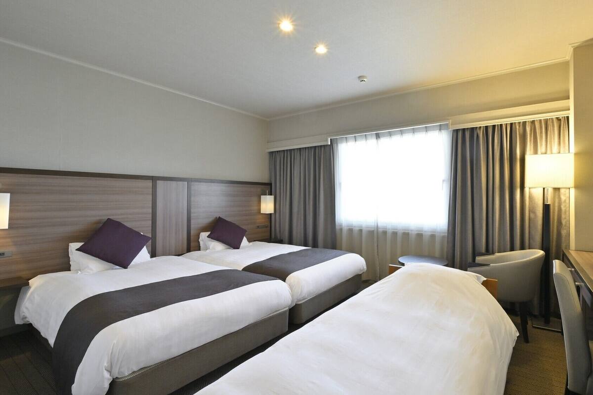 A hotel room with two beds, a desk, a chair, a TV, and a window with curtains.