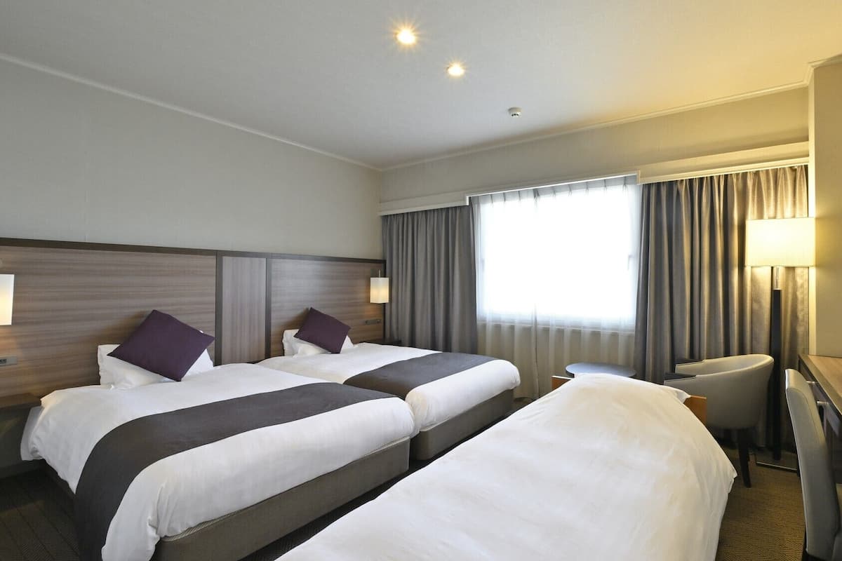 A hotel room with two beds, a desk, a chair, a TV, and a window with curtains.