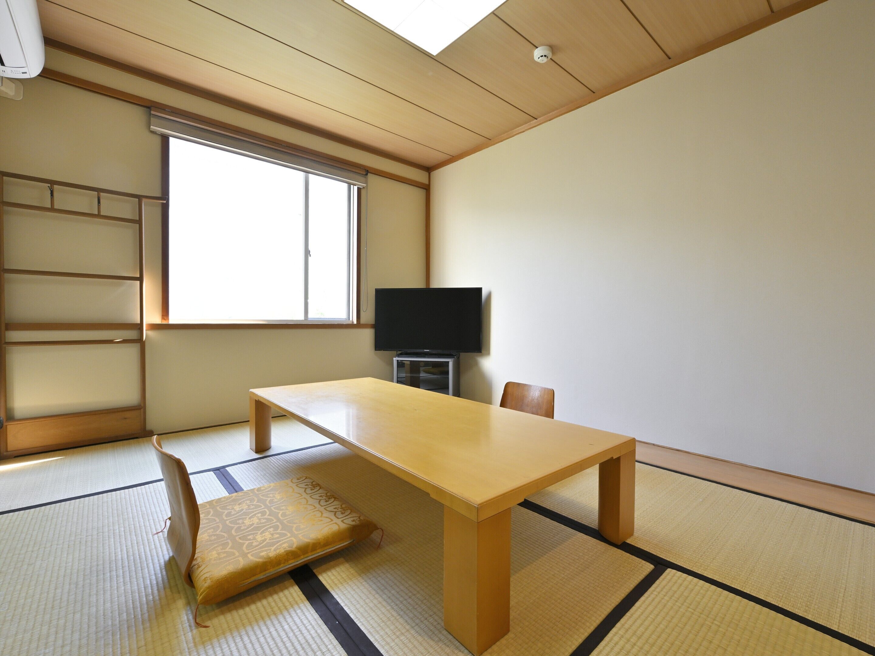 Una habitación con suelo de tatami, una mesa de madera, un televisor y una puerta corredera.