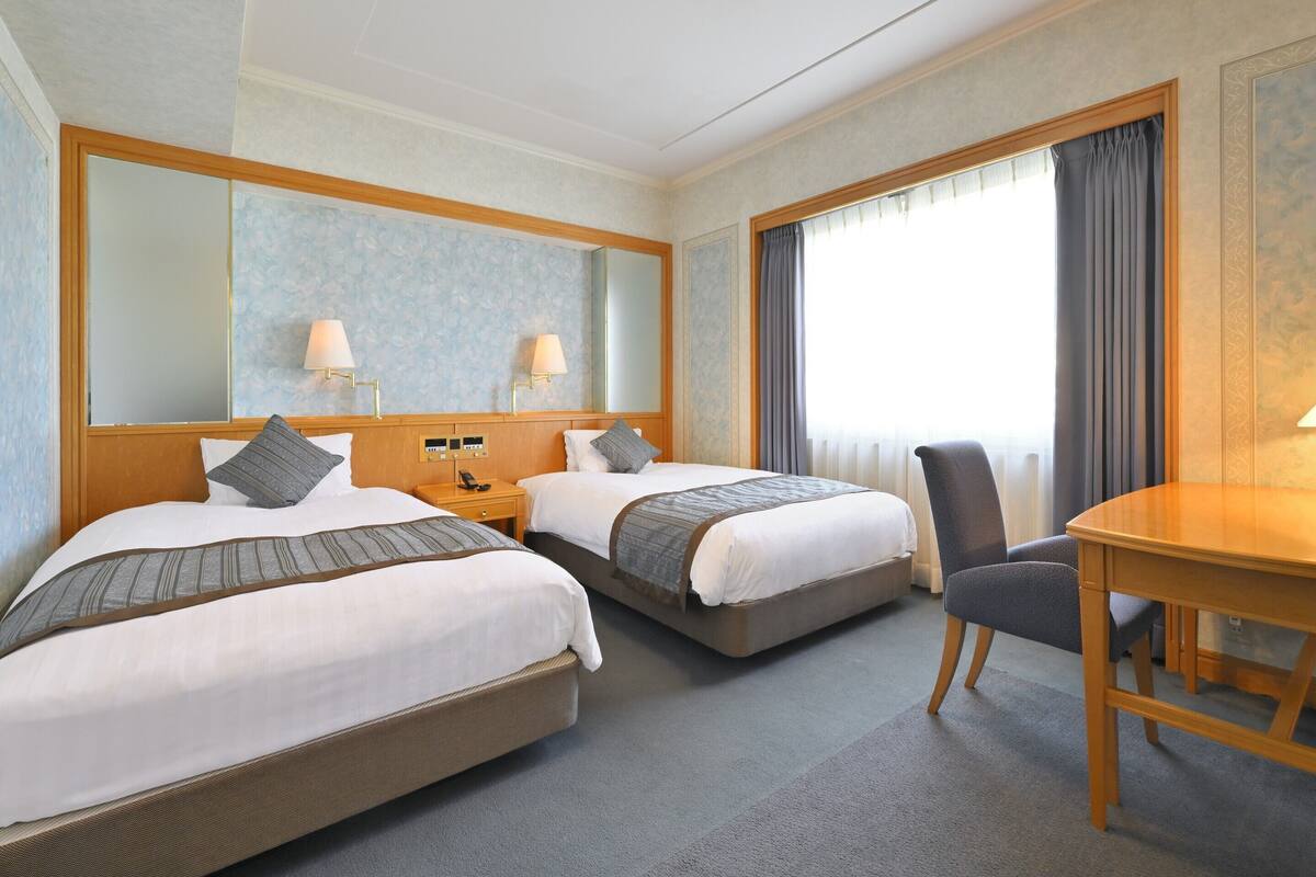 A hotel room with two beds, a desk, and a chair.