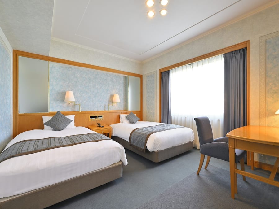 A hotel room with two beds, a desk, and a chair.